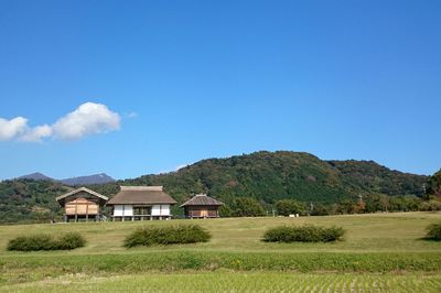 Houses on grassy field against cloudy sky