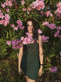 Beautiful young woman standing by pink flowering plants