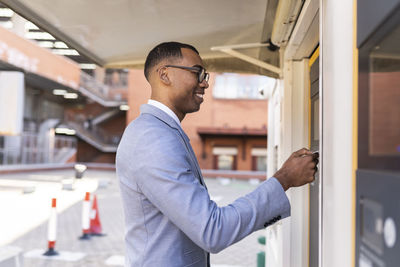 Smiling businessman wearing eyeglasses using ticket machine