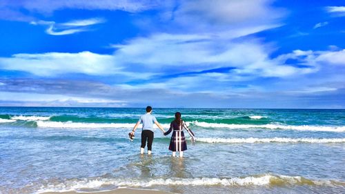 Rear view of couple standing at beach against sky