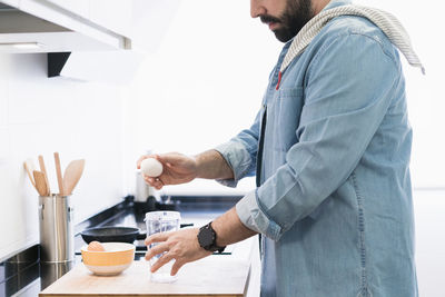 Man cooking in the kitchen in a denim shirt. an anonymous man is going to crack an egg