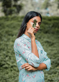 Portrait of young woman holding leaves while standing on field