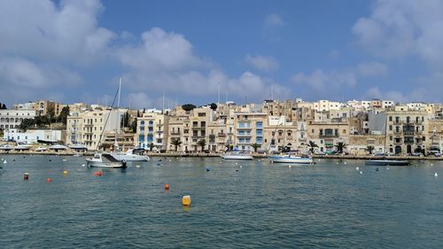 Boats in sea by buildings in city against sky