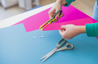 Cropped hands of woman cutting colorful papers on table