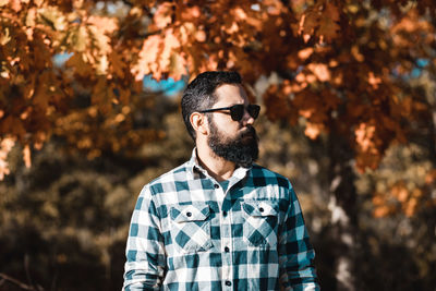 Bearded man looking away while wearing sunglasses against trees