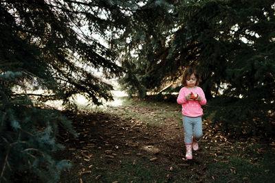 Young girl eating a red apple walking through a row of pine trees