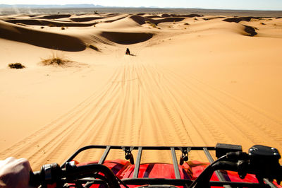 Cropped hand of man riding vehicle on sand at desert during sunny day