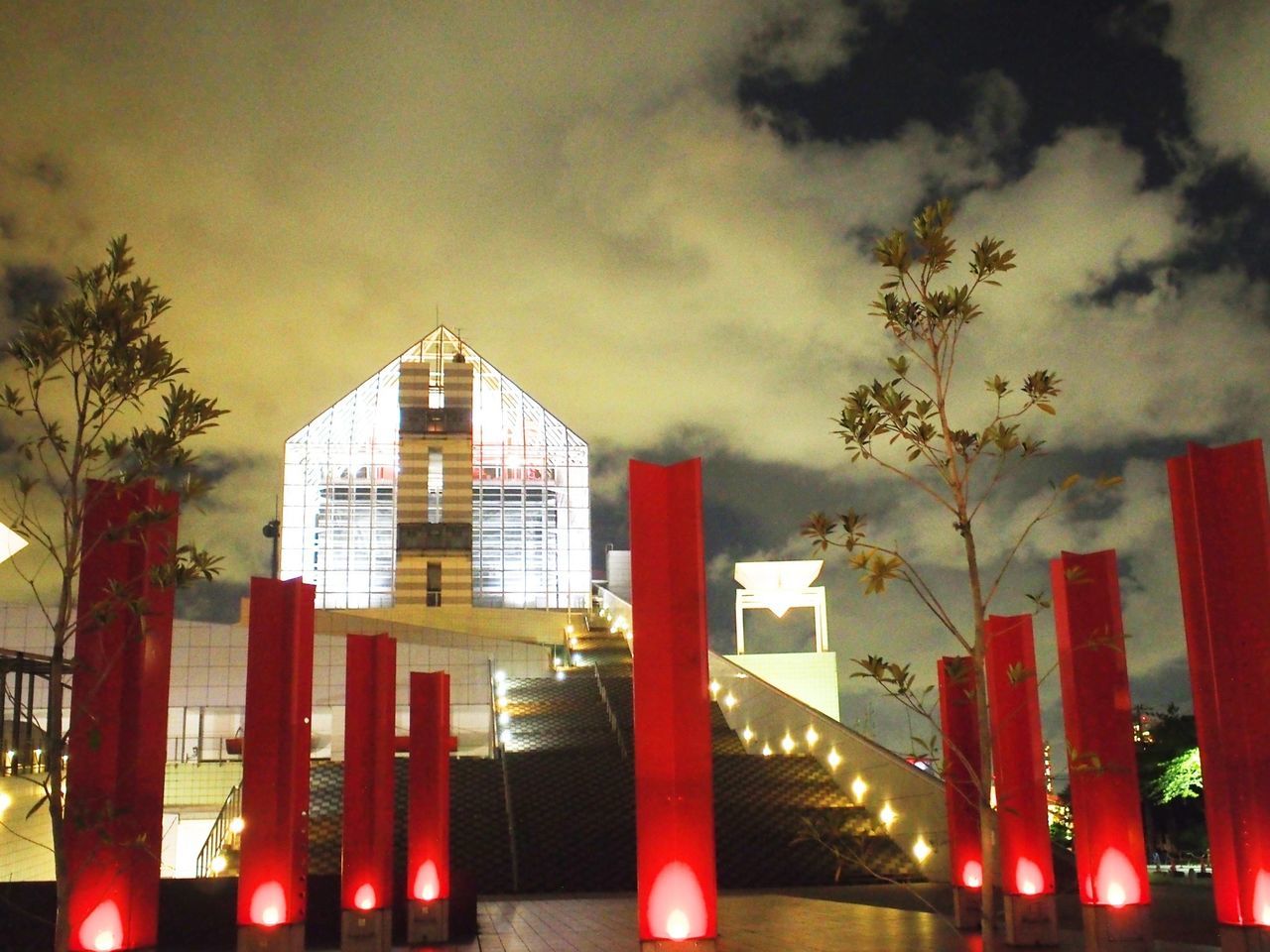 architecture, built structure, building exterior, sky, cloud - sky, red, tree, architectural column, city, low angle view, lighting equipment, illuminated, sunset, street light, cloudy, no people, outdoors, growth, building, cloud