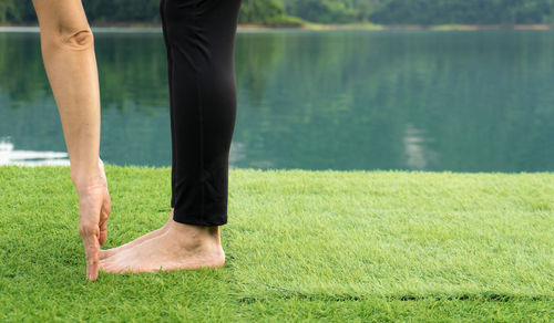 Low section of woman exercising on field by lake