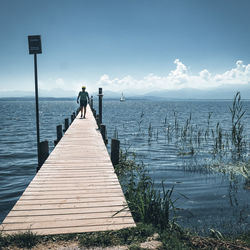 Rear view of woman standing on pier over sea against sky