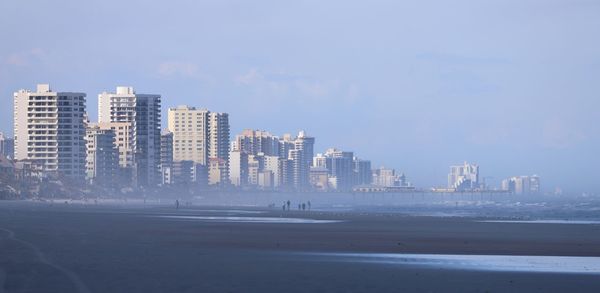 Modern cityscape by sea against sky