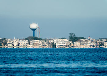 Buildings by sea against clear blue sky