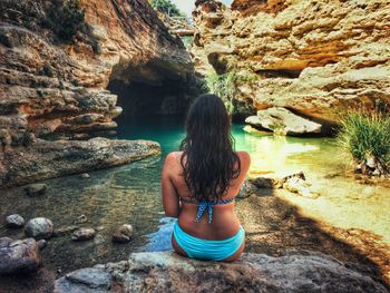 Rear view of woman sitting on rock formation