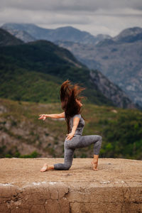 Side view full length of woman exercising on cliff against mountains