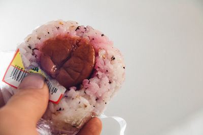 Cropped hand of person holding umeboshi with rice ball against wall