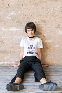 Portrait of young woman sitting against wall