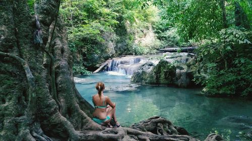 Rear view of woman sitting in front of lake at erawan national park