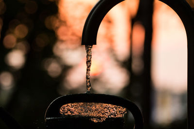 Close-up of water falling from faucet during sunset