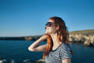 Woman wearing sunglasses standing against sea against clear sky