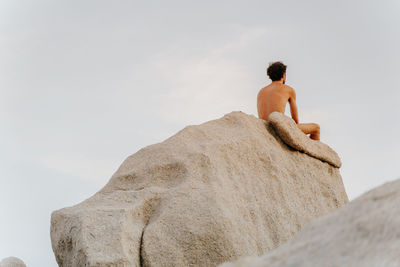 Rear view of naked man sitting on rock