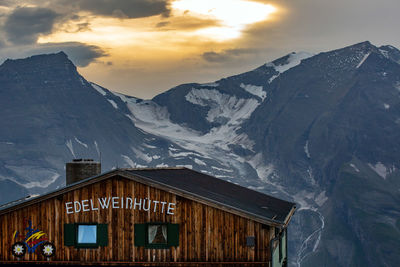 House on snowcapped mountain against sky during winter