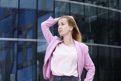 Young blonde woman with long hair in pink  clothes stands near a modern building 