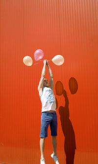 Man with balloons levitating against red wall