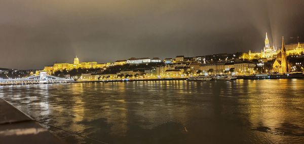 Illuminated city by river against sky at night