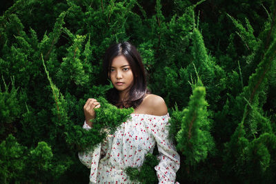 Portrait of beautiful young woman standing against plants