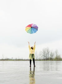 Beautiful brunette woman in yellow raincoat throwing colorful umbrella up in the rain