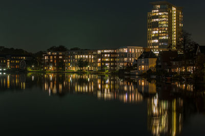 Illuminated buildings reflecting in river against sky at night