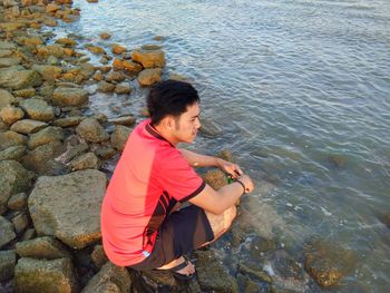High angle view of young man on rock at sea shore