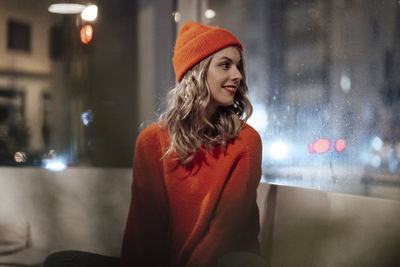 Smiling blond woman wearing knit hat looking through cafe window