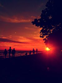 Silhouette people at beach against sky during sunset