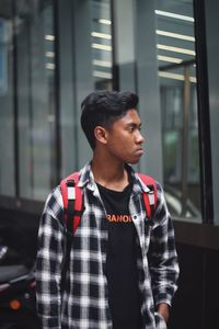 Young man looking away while standing against building