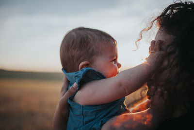 Close-up of mother carrying daughter against sky