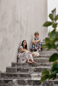Two women wearing summer clothes, sitting on stone stairs in old town