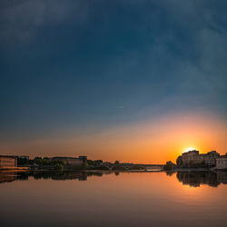 Scenic view of river by buildings against sky during sunset