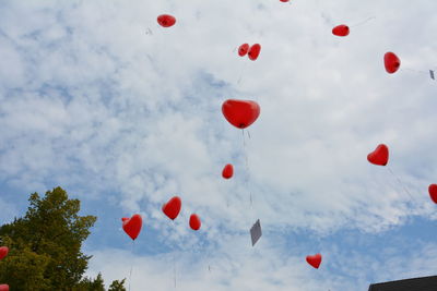 Low angle view of red heart shaped helium balloons flying in cloudy sky