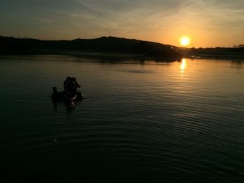 Silhouette people swimming in lake against sky during sunset