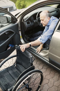 Disabled man pulling wheelchair while disembarking car on street