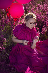 Portrait fashionable beautiful young woman sit in a purple dress in a field with wildflowers 