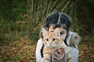 Portrait of girl holding cat against plants during autumn
