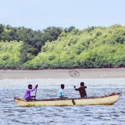 People sitting on boat in river against trees