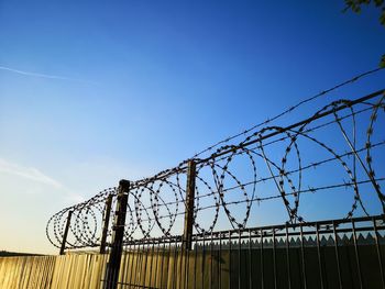 Low angle view of razor wire fence against blue sky
