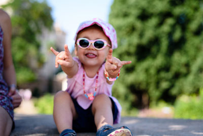 Portrait of happy girl gesturing horn sign while sitting outdoors