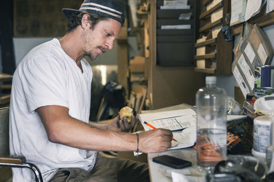 Side view of carpenter writing on document at table in workshop