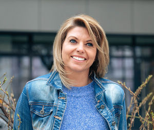 Woman in blue smiles brightly, standing outdoors in denim attire