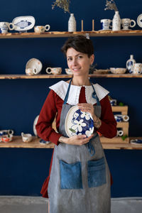 Successful ceramics studio owner posing with handmade plate at workplace