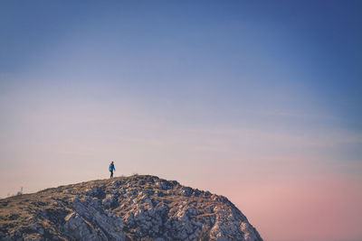 Person standing on cliff against clear sky during sunset